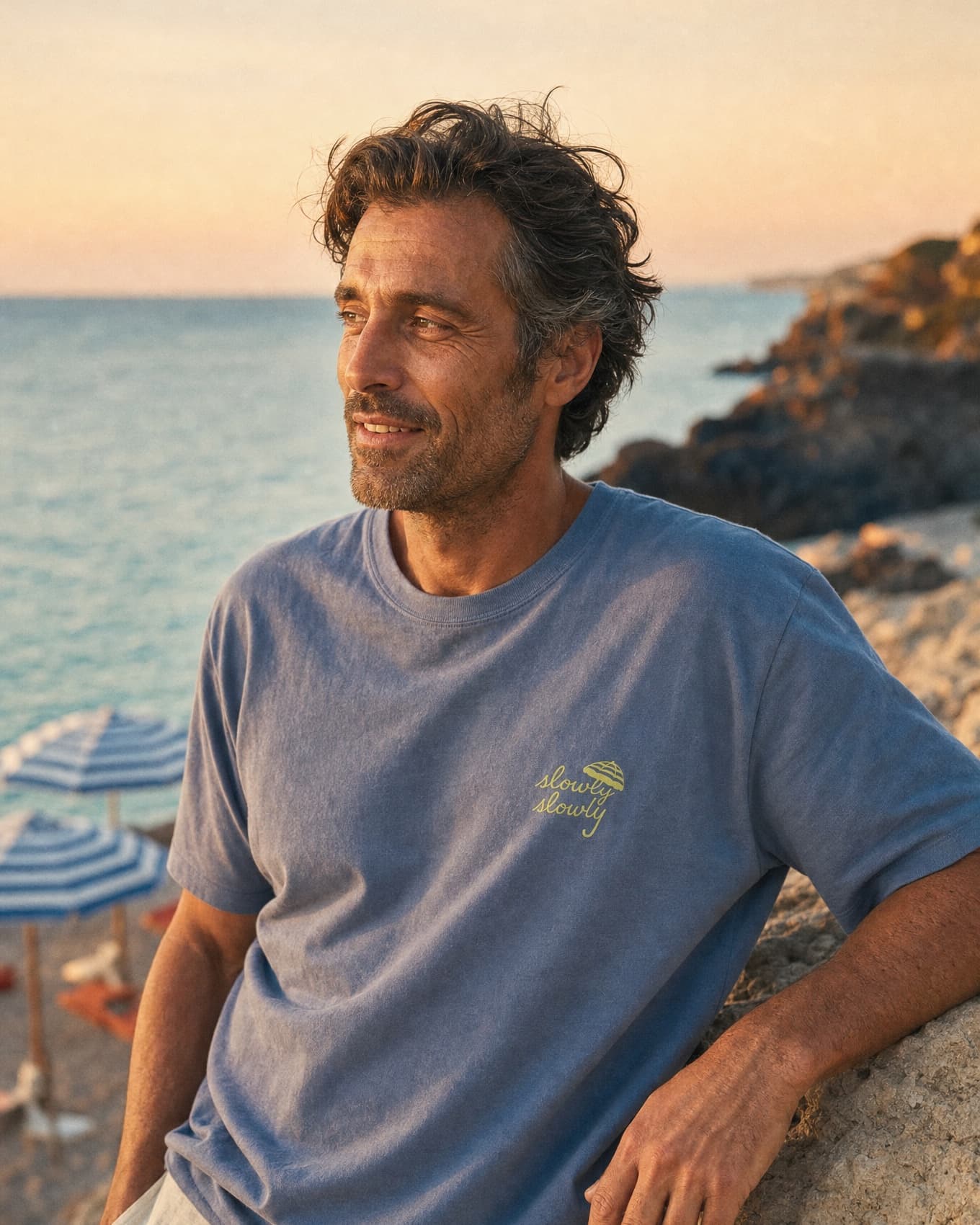 Amalfi Tee worn at the water's edge at golden hour, striped parasols behind