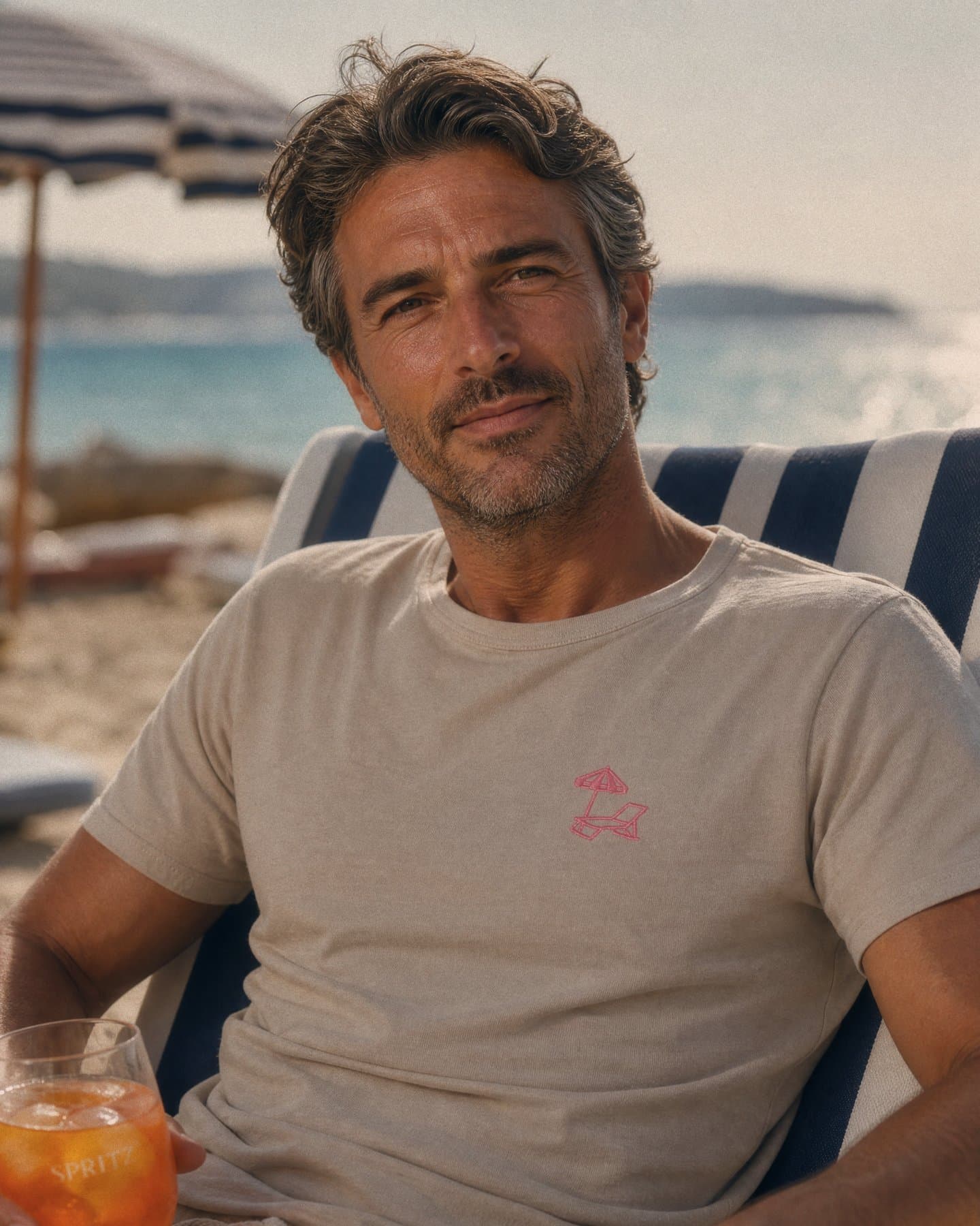 The Puglia Embroidery Tee worn on the beach with a spritz, pink chest embroidery visible