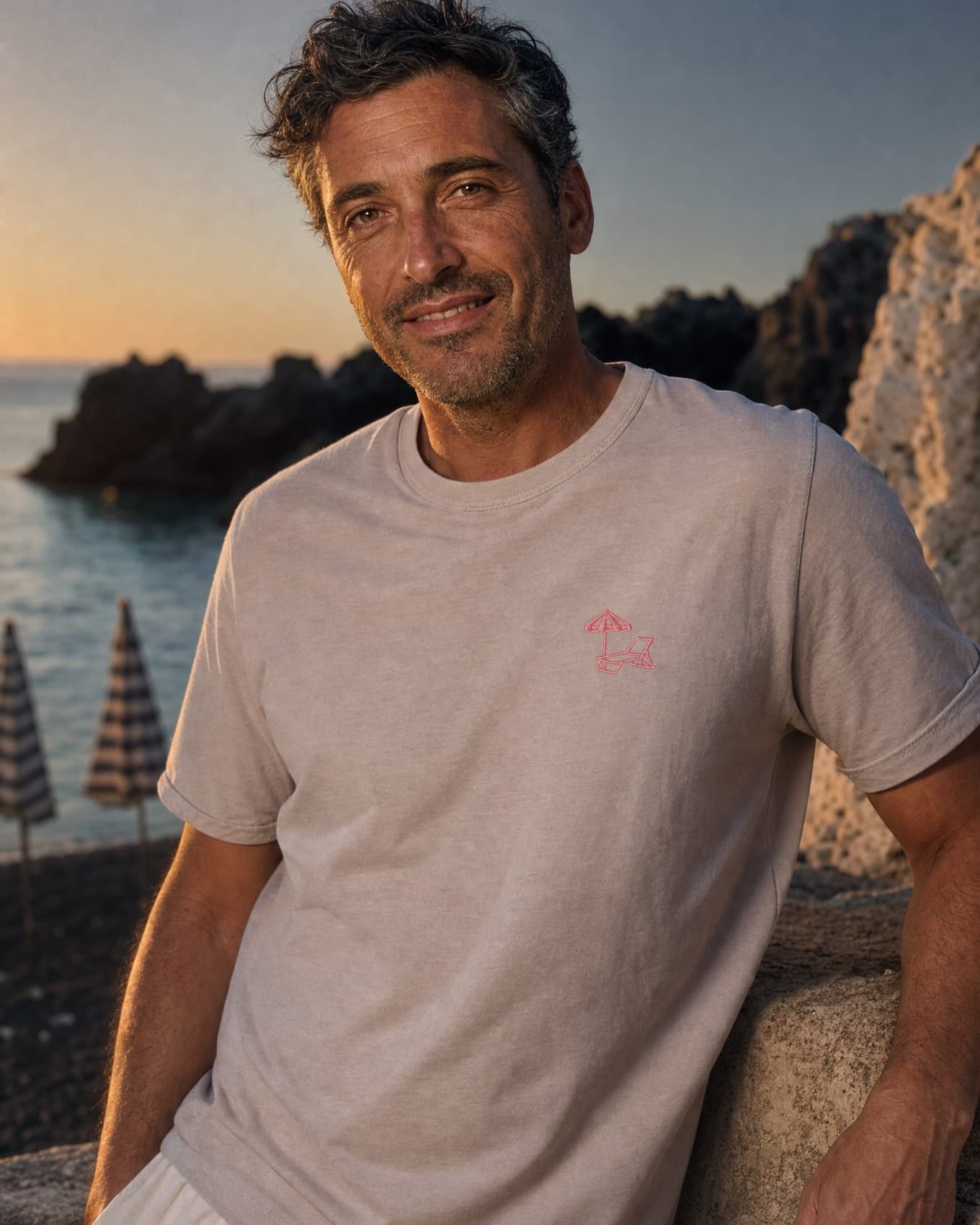 The Puglia Embroidery Tee worn on the rocks at golden hour, pink chest embroidery visible
